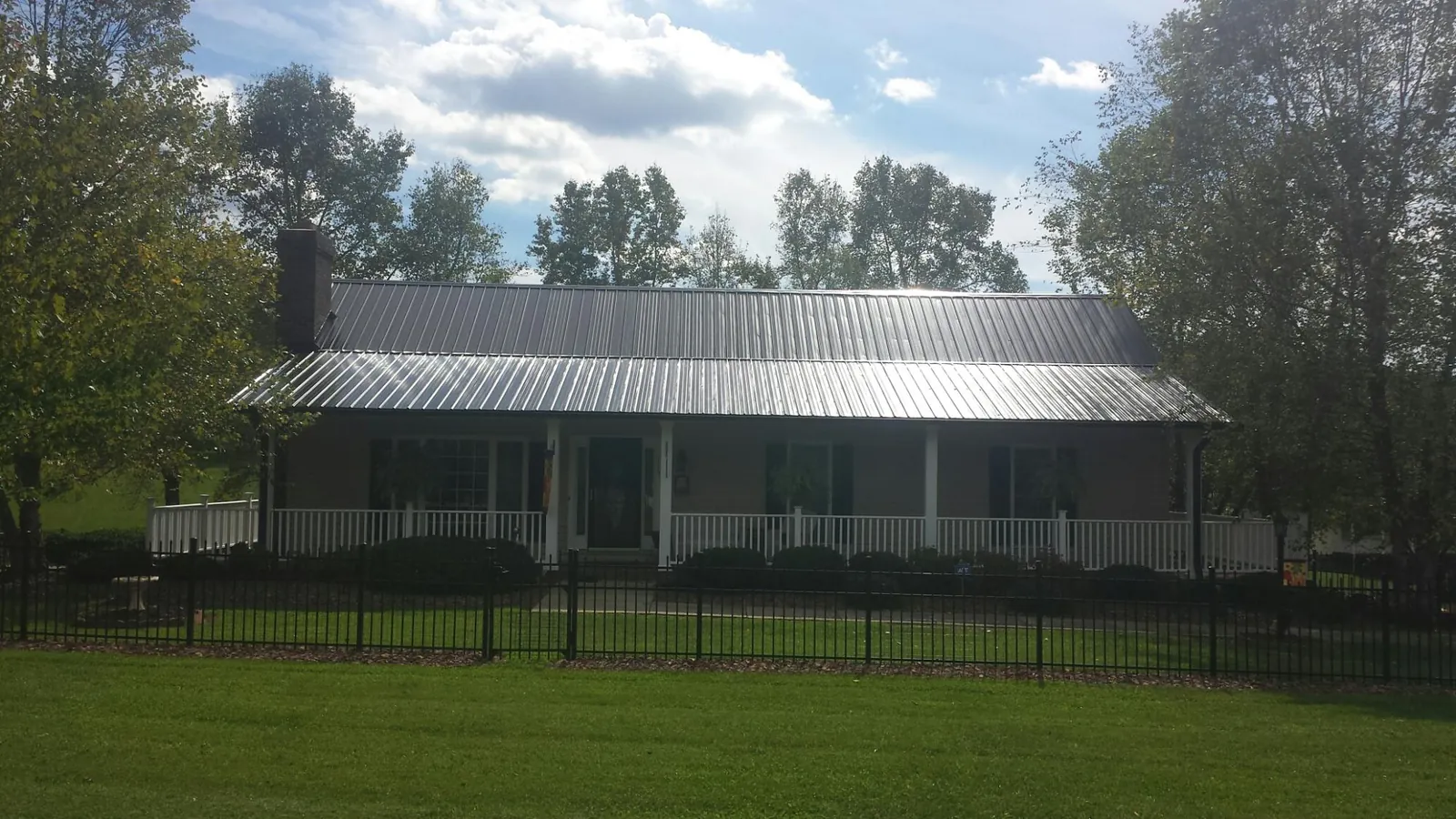 Gray metal roof on a brick ranch with a full width front porch — Gutter Guard Installation work by our crew in Rogers