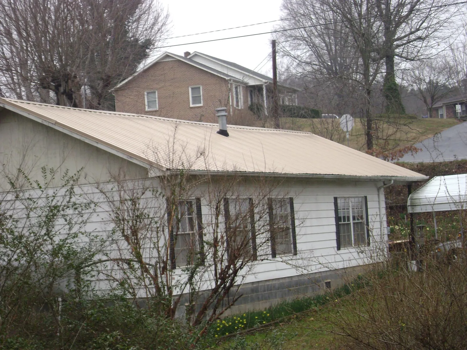 Tan metal roof on a white sided house set into a hillside — Commercial Roofing by Roofing Brothers in Rogers